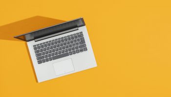 Gray laptop on a bright yellow desk and blank copy space, top view